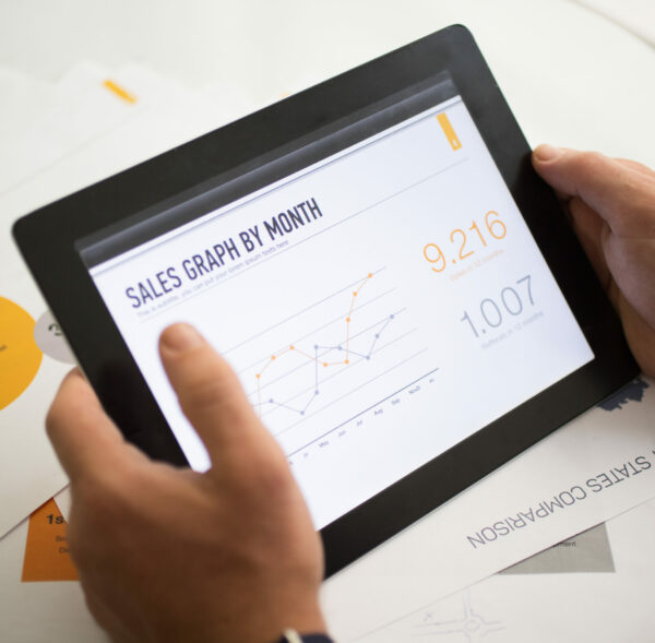 Sales graph on tablet screen. Close-up of analyst examining statistics. Unrecognizable businessman using digital tablet at table with papers. Progress concept